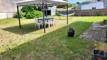 A covered outdoor seating area with a table and chairs, a hammock, and a potted plant.