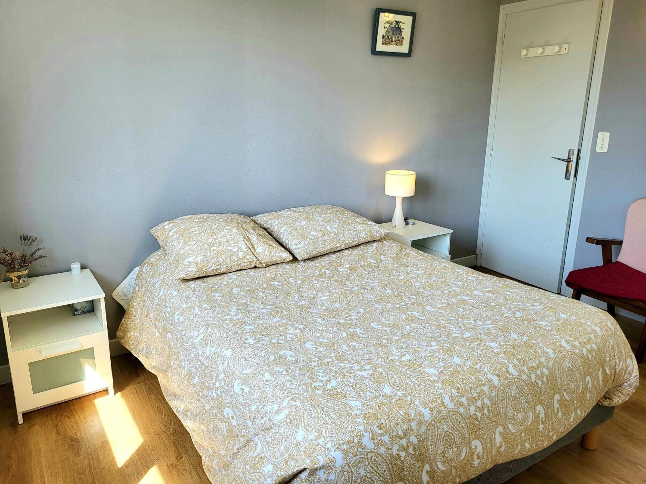 A neatly made bed with a patterned bedspread, a bedside lamp, a small bedside table, and a chair.