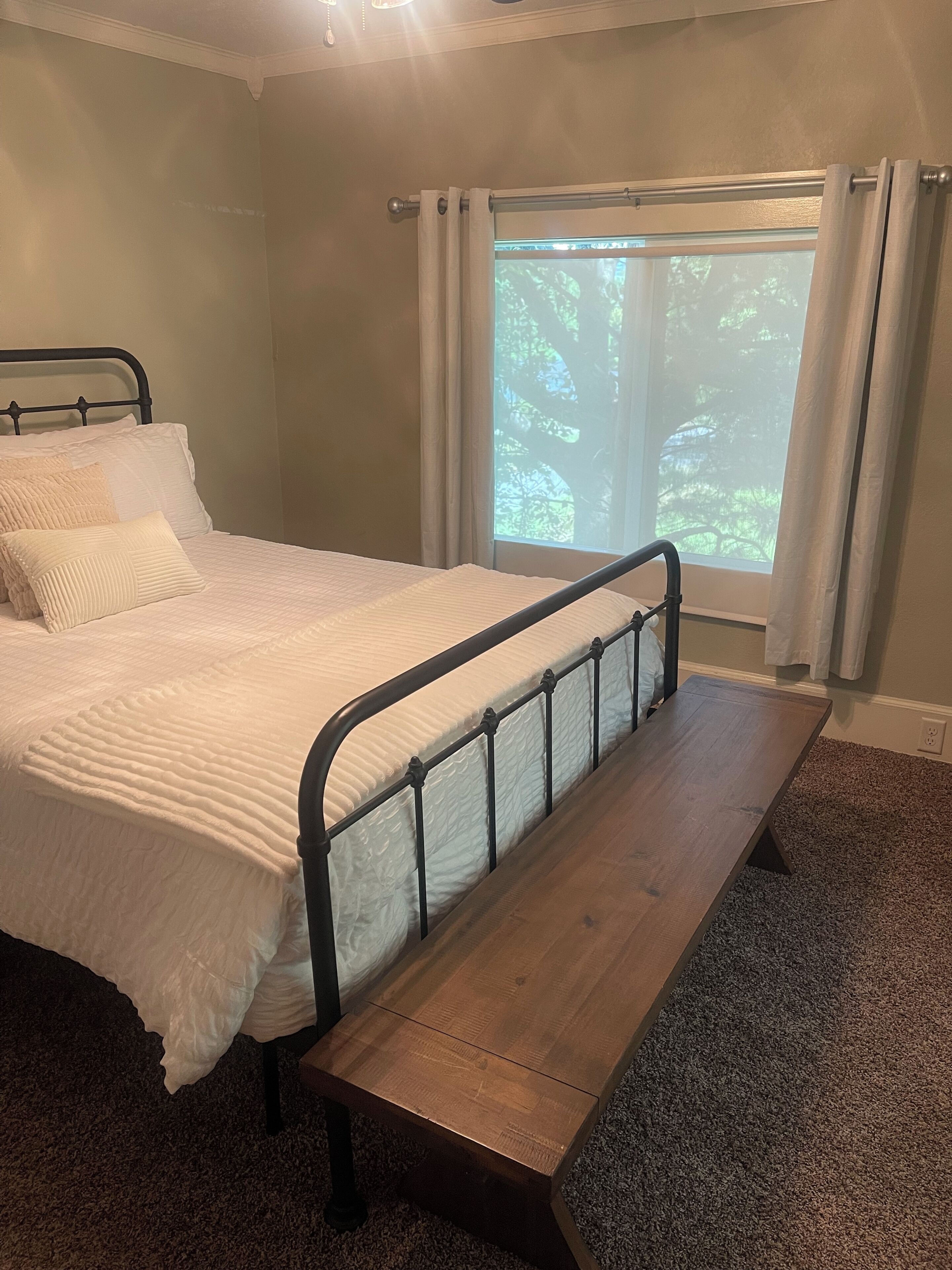 Een slaapkamer met een bed, een houten bankje, een raam met gordijnen en een vloerbedekking.