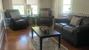 Uma sala de estar com um sofá de couro escuro, duas poltronas de couro, uma mesa de centro e um tapete estampado.
