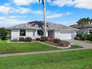 A single-story house with a grey roof, white exterior walls, a front porch, and a driveway. - Coastal Waterfront Home With Pool spa and Dock (Marco Island)