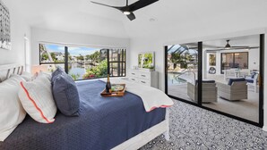 Ein modernes Schlafzimmer mit Bett, Deckenventilator, großem Fenster und Blick auf einen Außenpool.