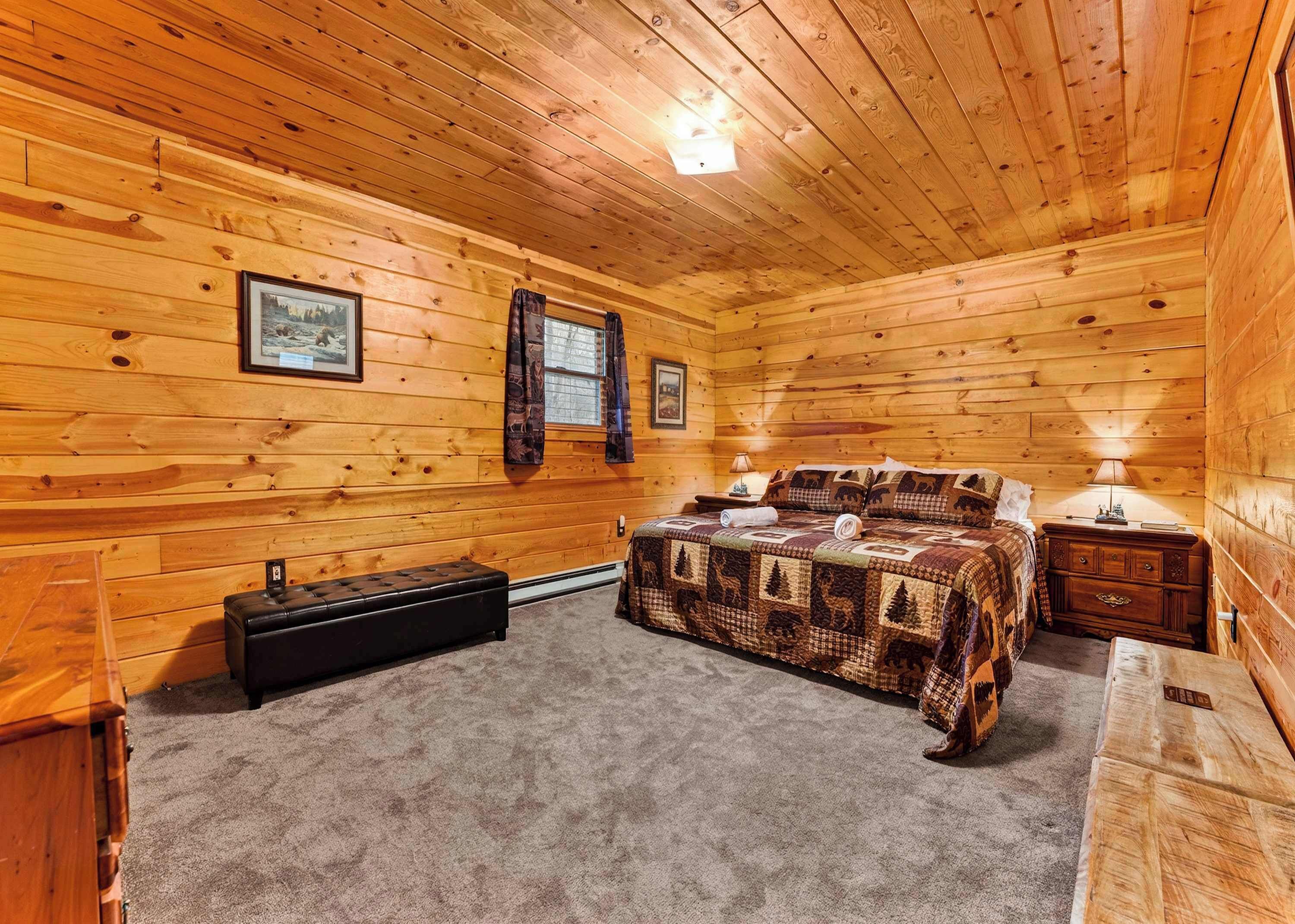 Een slaapkamer in een houten blokhut, met een bed, nachtkastjes, een bankje en een koffer.