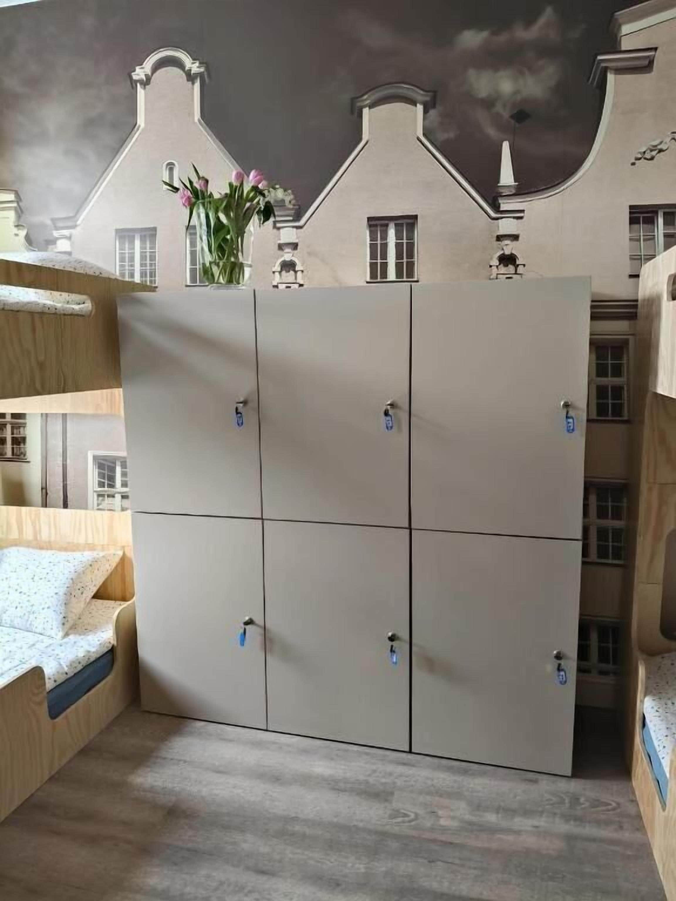 Un lit superposé avec une tête de lit en bois, une armoire avec un miroir et une fresque murale représentant un bâtiment.