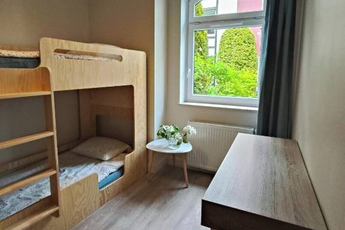 A room with a bunk bed, a small table, and a window with a view of greenery.
