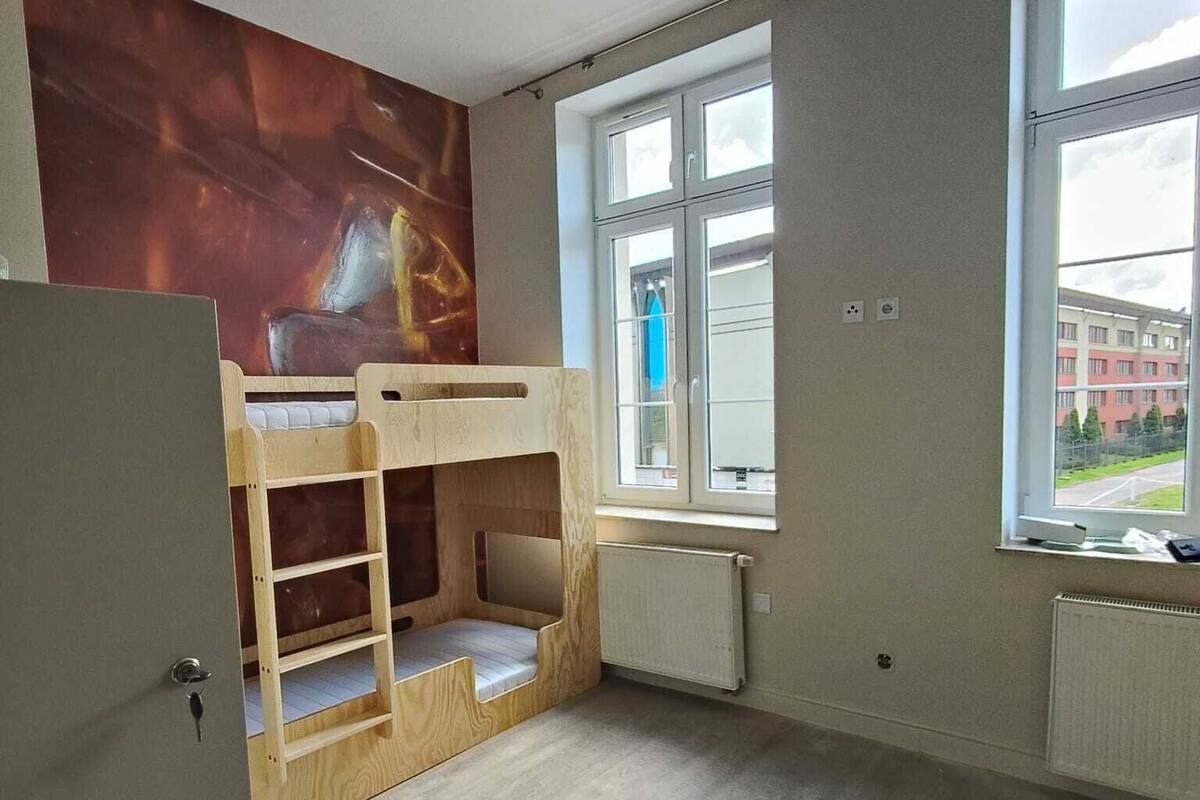 A room with a bunk bed, a radiator, a window with a view of buildings, and a door.