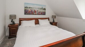 Een slaapkamer met een bed, twee nachtkastjes, een schilderij en een schuine plafond.