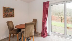 Een eethoek met een ronde tafel en stoelen, een plafondlamp, een raam met uitzicht op de omgeving en een lijst met een afbeelding aan de muur.