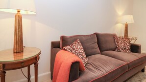 En brun sofa med røde detaljer, to puder med mønster og et sofabord med glasplade og lampe.
