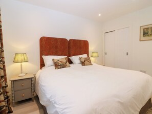 A neatly made bed with white bedding, two bedside lamps, and a patterned headboard. - East Camno Farm Cottage (Blairgowrie)