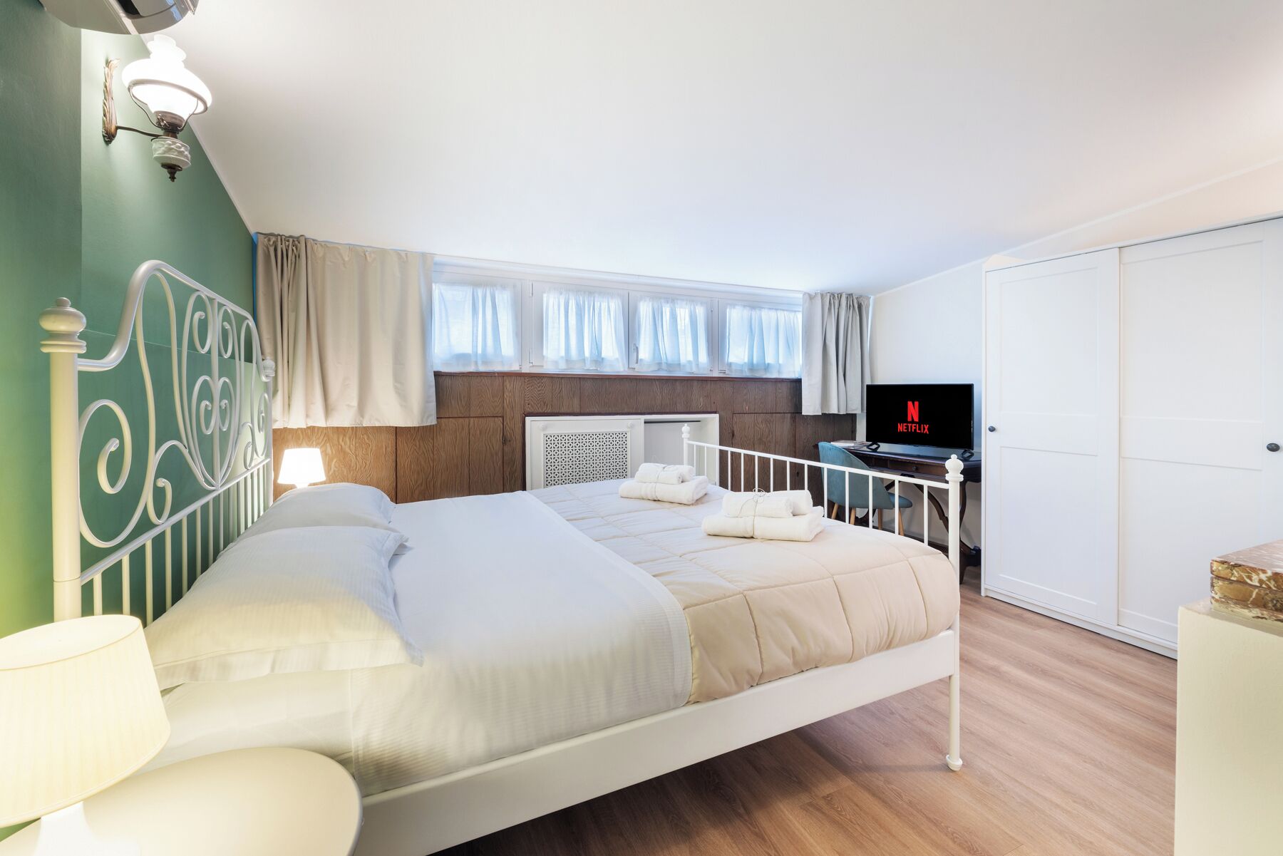 A neatly arranged bedroom with a bed, bedside lamps, a TV, and a wardrobe.