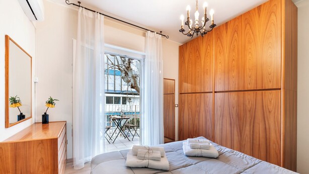 Een slaapkamer met een bed, een houten garderobe, een spiegel en een kroonluchter.