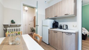 Een kleine keuken met een koelkast, koffiezetapparaat en waterkoker op het aanrecht.