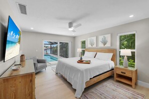 A bedroom with a bed, a TV, a desk, a chair, a nightstand, and a window with a view of a pool. - 737 Nautilus Court (Marco Island)