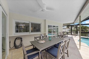 An outdoor patio with a table and chairs, a ceiling fan, and a view of a swimming pool. - 737 Nautilus Court (Marco Island)