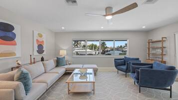 A modern living room with a sofa, armchairs, a coffee table, and a ceiling fan.