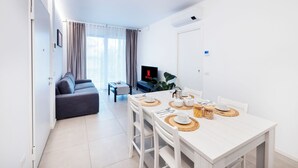 A modern living room with a sofa, a dining table set with placemats, and a TV displaying the Netflix logo. - Cattolica Modern Beach - Riviera Collection (Cattolica)