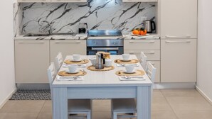 A modern kitchen with white cabinets, a marble backsplash, and a dining table set for four. - Cattolica Modern Beach - Riviera Collection (Cattolica)