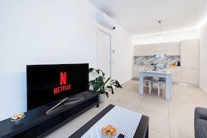 A modern living room with a flat-screen TV displaying the Netflix logo, a dining area with a white table and chairs, a kitchen with marble countertops, and a potted plant. - Cattolica Modern Beach - Riviera Collection (Cattolica)