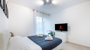 A modern hotel room with a bed, a flat-screen TV, a potted plant, and a window with curtains. - Cattolica Modern Beach - Riviera Collection (Cattolica)