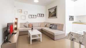 Un salon moderne avec un canapé d’angle, une table basse blanche, un téléviseur à écran plat et un tableau accroché au mur.