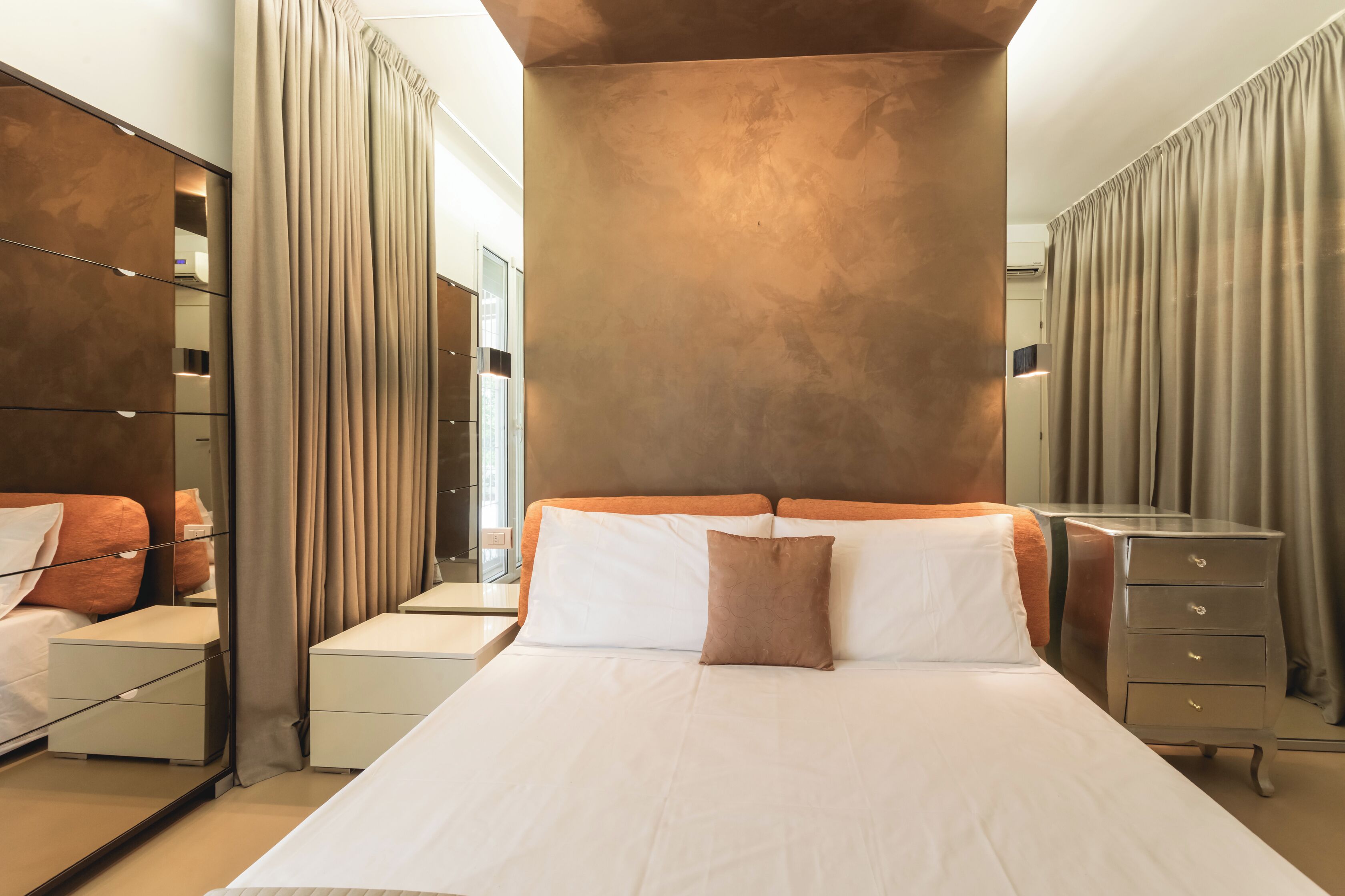 Una habitación de hotel moderna con una cama grande, una mesita de noche, un aparador y un espejo.