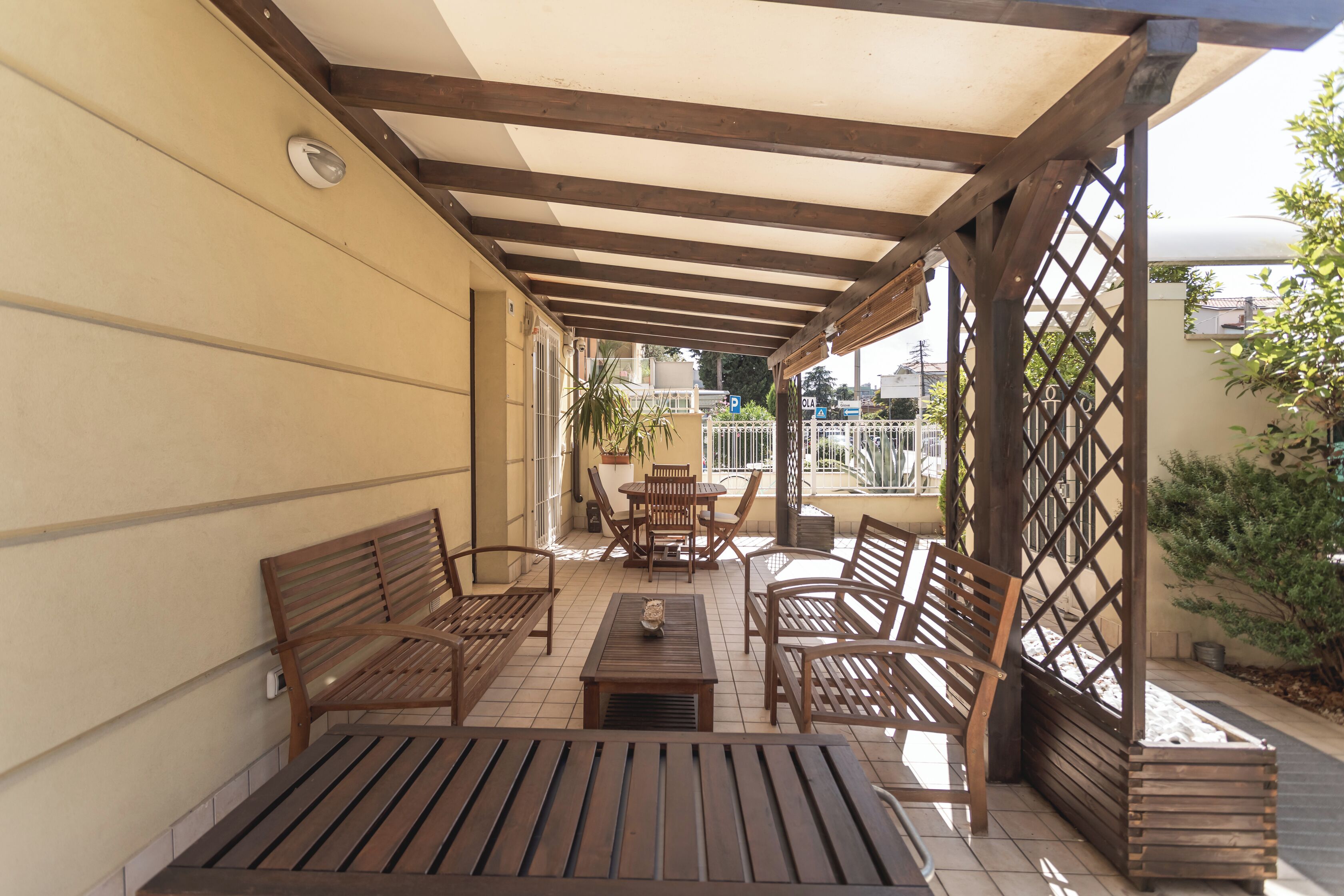 An outdoor patio with wooden furniture, a pergola, and a view of the street.