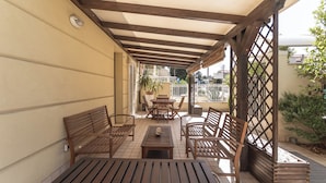 Une terrasse extérieure avec des meubles en bois, une pergola et une vue sur la rue.