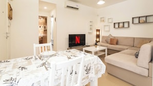 Un salon avec un téléviseur, un canapé, une table à manger et une cuisine en arrière-plan.