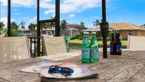 Et træbord med et magasin, solbriller og flasker med Pellegrino og Spella vand.