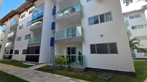 A multi-story residential building with balconies, large windows, and a paved walkway. - Novo Torres do Porto 202B by La Playa  (Ipojuca)
