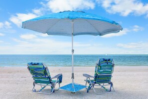 Two beach chairs under a blue umbrella on a sandy beach with the ocean in the background. - Marco Beach Ocean Resort 910 (Marco Island)