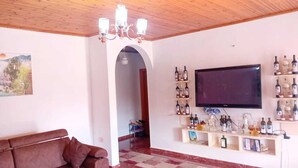 Un salon comprenant un canapé, un lustre, un téléviseur fixé au mur et des étagères remplies de bouteilles.