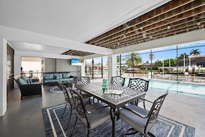 A poolside dining area with a table and chairs, a sofa, and a TV screen. - 1672 Barbarosa Court (Marco Island)
