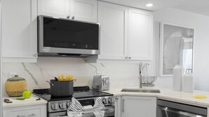 A modern kitchen with white cabinets, a stainless steel stove, a microwave, and a toaster. - Sea Winds 1404 (Marco Island)