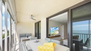 A balcony with a dining table, a sofa, and a TV. - Sea Winds 1404 (Marco Island)