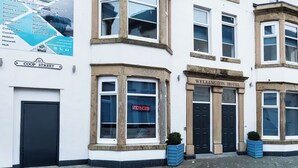 Un hôtel à deux étages, avec une enseigne indiquant « The Wellington Hotel » et une autre, sur les fenêtres, indiquant « Chambres disponibles ».