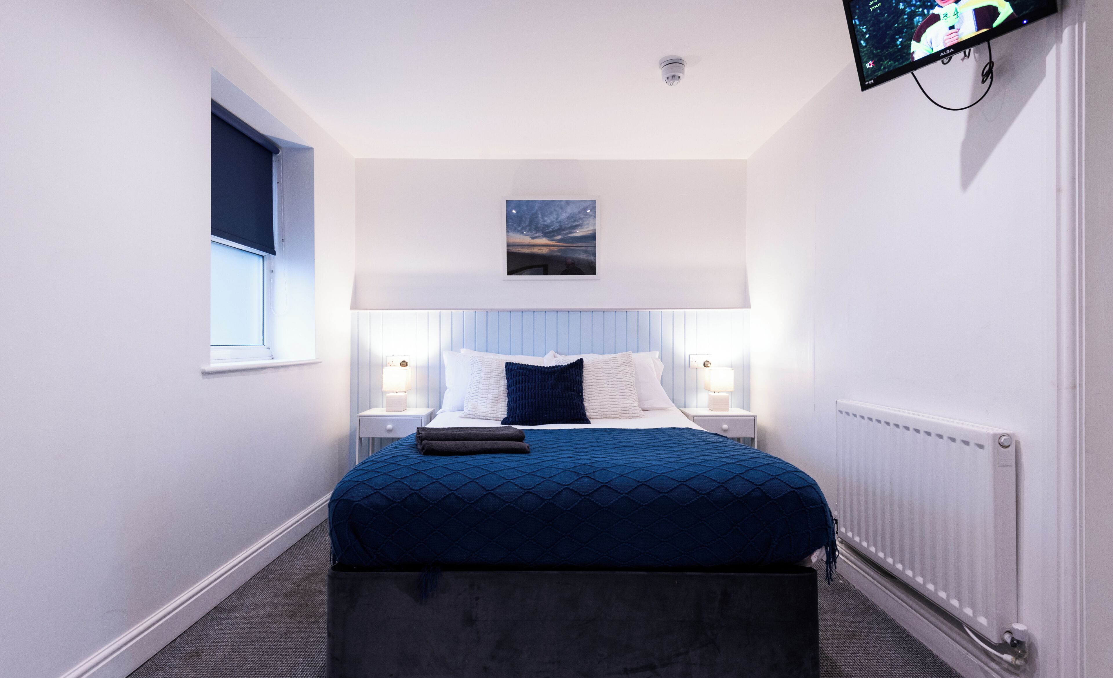 A bedroom with a bed, bedside tables, a window, a mounted TV, and a ceiling light.