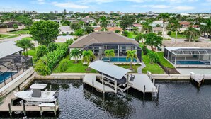 A residential area with a modern house featuring a swimming pool, a dock with a boat, and a clear view of the surrounding neighborhood. - 811 Apple Court (Marco Island)