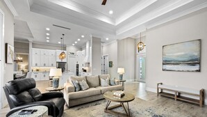 A spacious living room with a leather sofa, a coffee table, and a dining area with a chandelier. - 811 Apple Court (Marco Island)