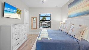 A bedroom with a bed, a dresser, a ceiling fan, a TV, a window with a view, and a painting. - 811 Apple Court (Marco Island)