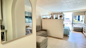 Ein großzügiger Wohnbereich mit einem großen Spiegel, einem grauen Sofa, einem weißen Teppich und Blick auf den Außenbalkon.