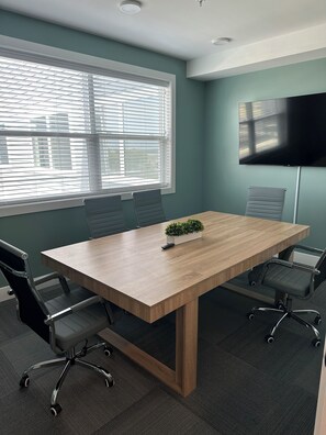 Ett konferensrum med ett träbord, svarta kontorsstolar, en krukväxt och en platt-TV på väggen.