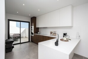 Une cuisine moderne avec un plan de travail blanc, un four encastré et une porte-fenêtre coulissante donnant sur un balcon.