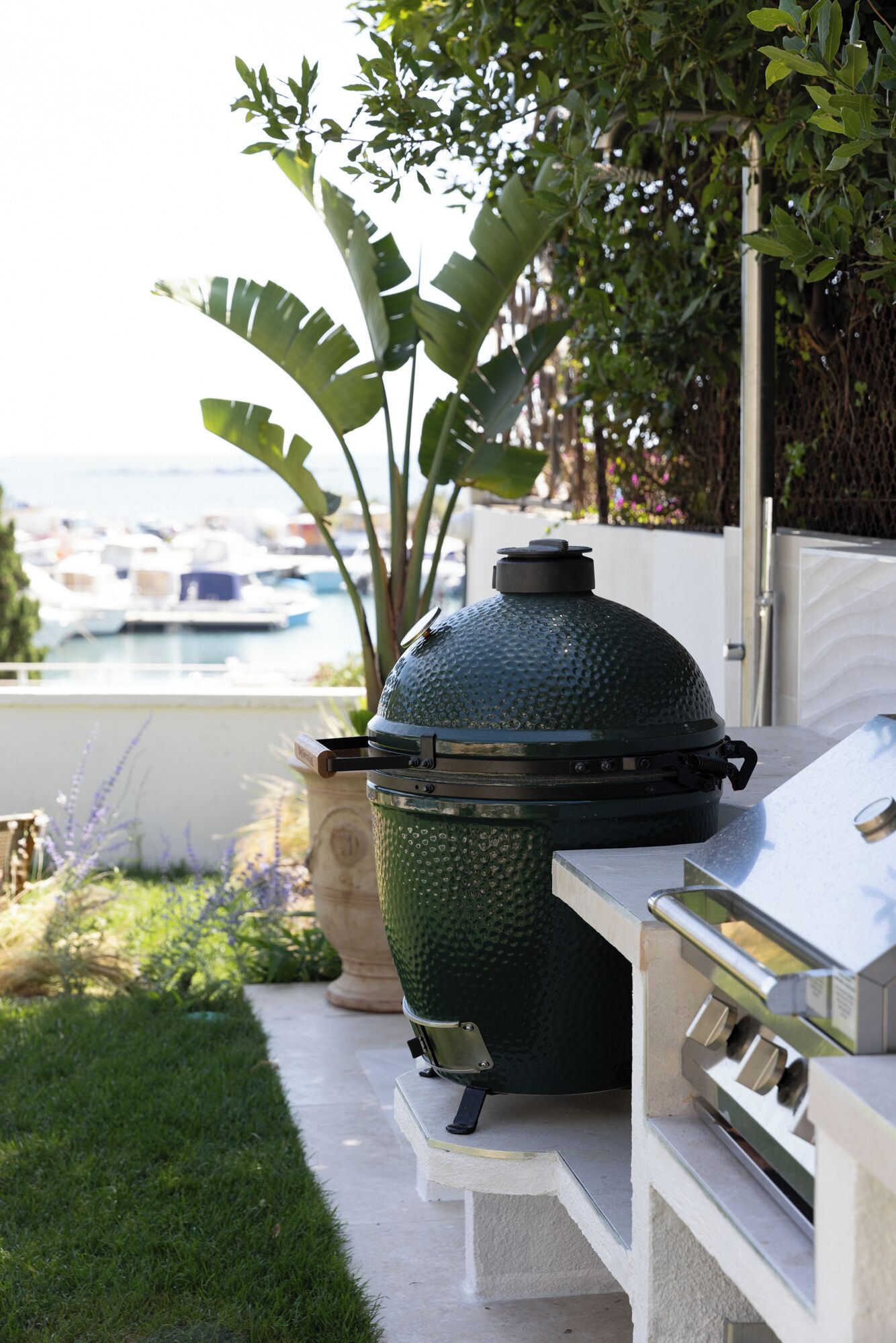 Ein Grill mit Deckel, ein Gasgrill und ein Blumentopf in einem Garten.