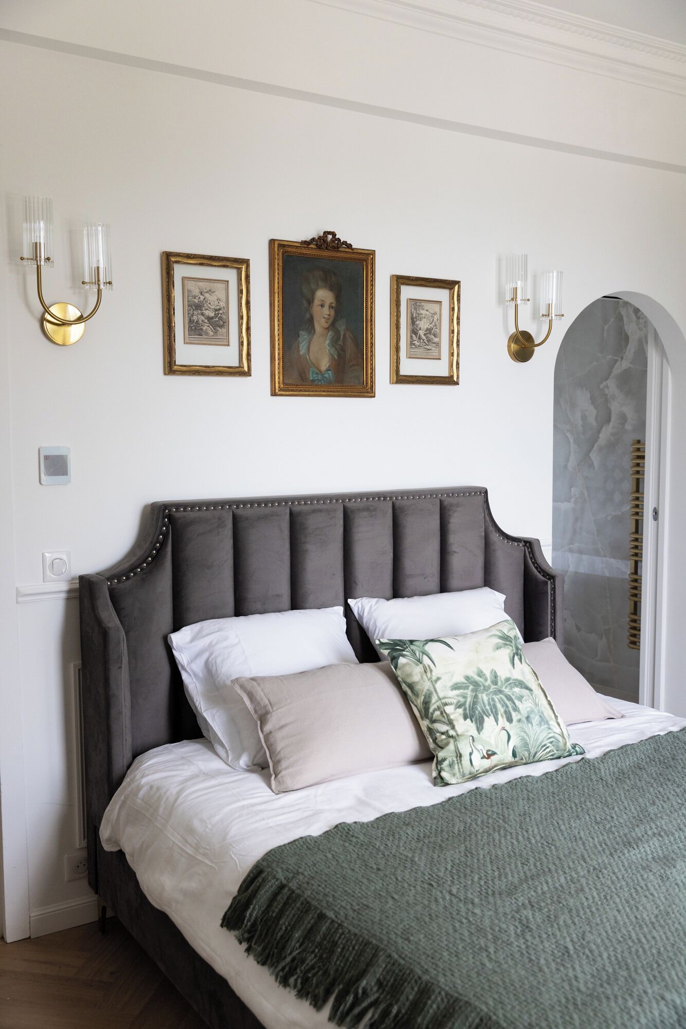 Ein Schlafzimmer mit einem großen Bett, einem grauen gepolsterten Kopfteil und drei gerahmten Kunstwerken an der Wand.