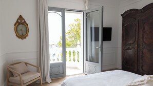 Quarto com cama, guarda-roupa de madeira, cadeira, televisão e varanda com vista.