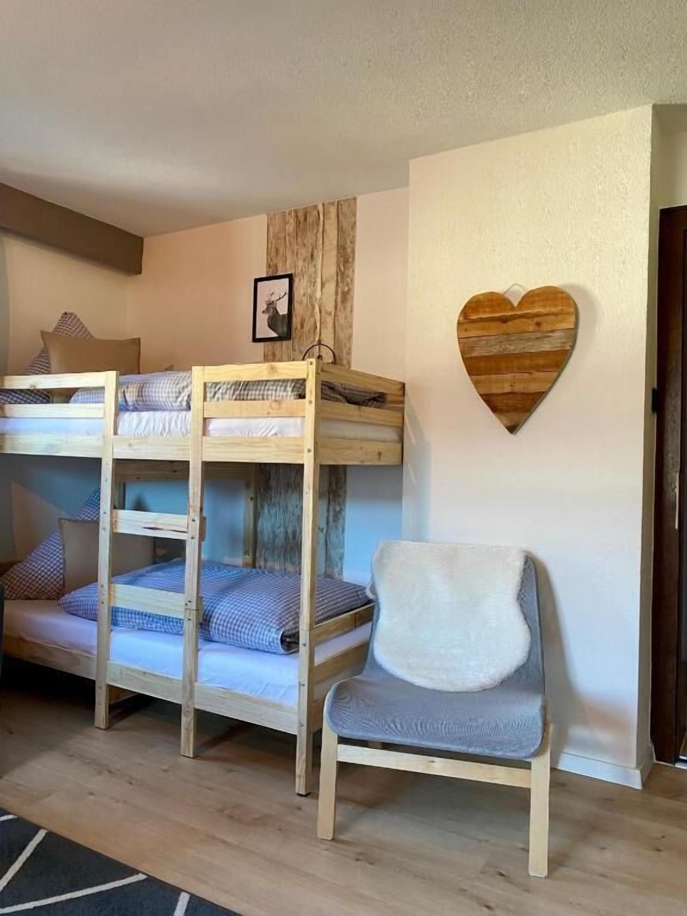 Un lit superposé avec une tête de lit en bois, un tableau représentant un cerf encadré et une décoration en bois en forme de cœur accrochée au mur.