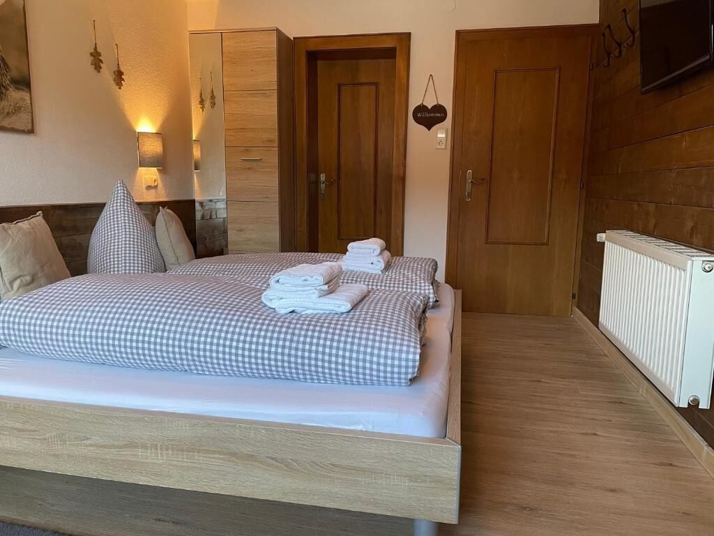 A neatly made bed with checkered bedding, a bedside lamp, a wall-mounted TV, and a 'Welcome' sign.