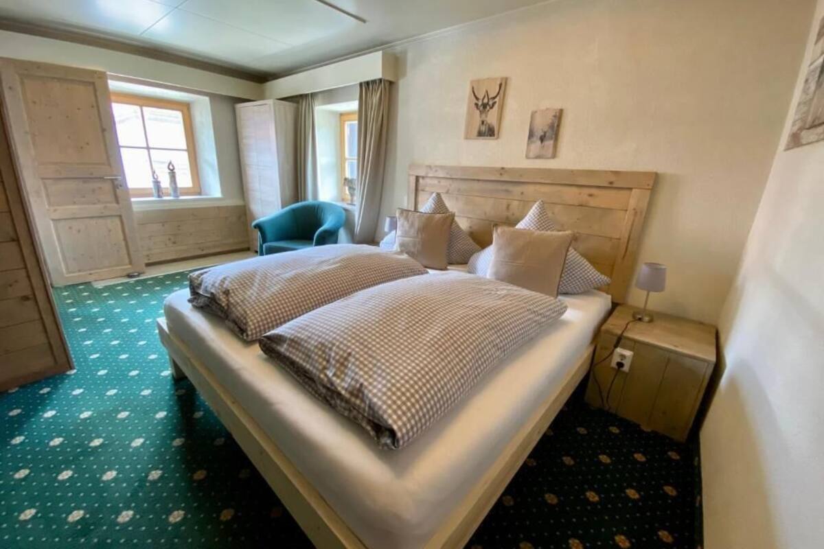 A hotel room with a large bed, a chair, a nightstand, and a window with curtains.